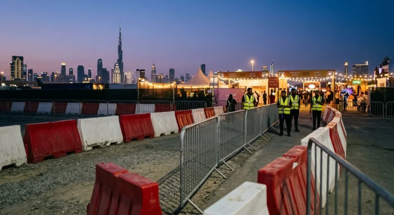 Crowd control and water-filled barriers forming the entry lane and perimeter of an outdoor evening event in Dubai